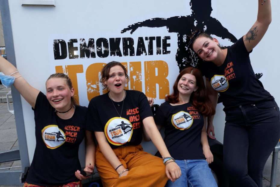 Vier motovierende junge Frauen vor dem Schriftzug Demokratietour Uckermark